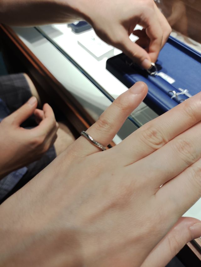 見本の指輪が薬指に入らず小指で試着する図